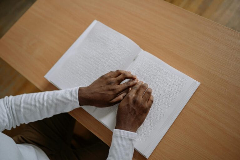 Close-up of hands reading braille in a book, symbolizing visual impairment awareness.